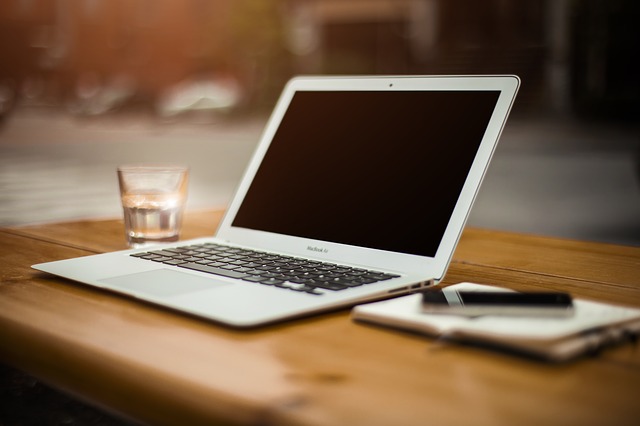 Laptop med ett gals vatten till vänster och ett skrivblock med penna till höger om den.