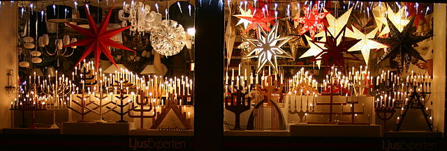 Upplyst skyltfönster fyllt med adventsstjärnor och adventsljusstakar